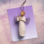 Willow Tree Just for You Ornament, 4”h hand-painted resin angel ornament in cream dress with wire wings, holding wire circle with 'thank you' written in wire, laying on lavender painting