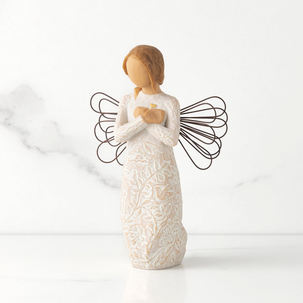 Front view of standing angel in cream dress with wire wings, crossed hands under small gold-leaf heart, dress carved with symbols of nature
