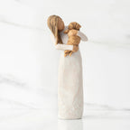 Front view, standing female figure in cream dress, holding golden color puppy in her arms