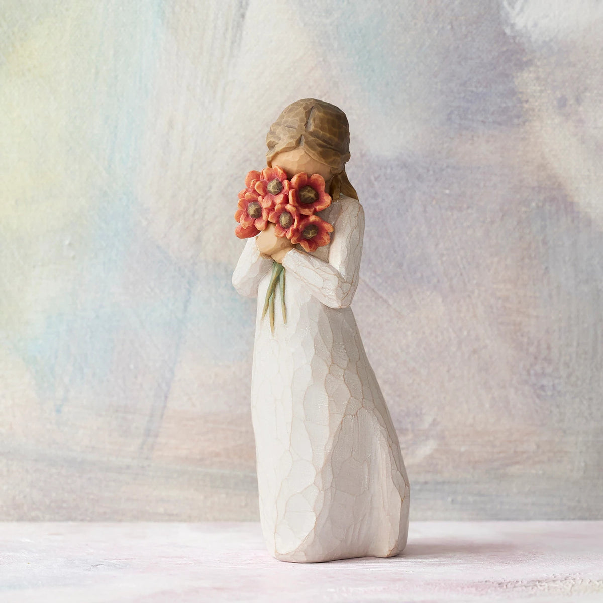 Willow Tree Surrounded by Love, 5"h hand-painted standing resin figure in cream dress, holding large bouquet of red-orange poppies up to face, in front of pastel painting