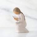 Side view of kneeling female figure in cream dress, with wire butterfly on extended hands, on marble background