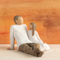 Willow Tree Father and Daughter, 5”h hand-painted resin figure of seated man dressed in neutral colors, legs outstretched, daughter in cream dress by his side, in front of sienna painting