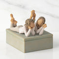 Front/long side view of closed rectangular blue-gray resin box, box; sculpture of two reclining girls on box lid