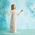 Willow Tree Everyday Blessings, 6.5”h hand-painted standing resin figure with bent elbows and arms raised, cream dress carved with nature symbols and gold-leaf dots, in front of aqua painting