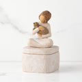 Front: cream square resin box with lid, 3-D figure of seated girl holding cat atop lid