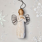 Willow Tree Remembrance Ornament, 4.5”h hand-painted resin angel figure in cream dress carved with symbols of nature, wire wings, crossed hands under small gold-leaf heart, brown elastic cord, laying amongst snowflakes