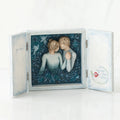 Open light wooden book with three parts - center is blue sky with two carved in faceless boy and girls hugging one another