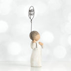 Small boy figurine facing the side in white holding up black wire balloon