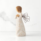 Left side view of standing female figure with wire wings in cream dress carved with natural symbols, hands crossed under gold heart on chest