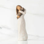 Left view, standing female figure in cream dress, holding dark color puppy in her arms