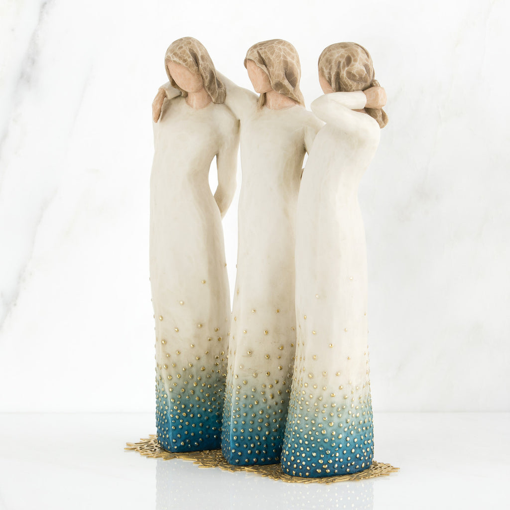 Three brown haired woman figurines with white dresses and blue bottoms with arms on each other