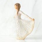 Left view of standing female figure in cream dress, holding out her skirt, which is carved with butterfly markings and dotted with gold
