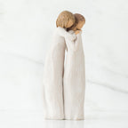 Two woman figurines in white dresses hugging one another facing the side