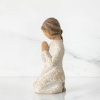 Small brunette girl figurine in white dress kneeling with hands folded - side view