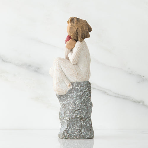 Side view of young girl in white sitting on grey rock with her hands up to her face