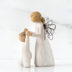 Side view of blonde angel figurine in white dress holding up baby figurine in white