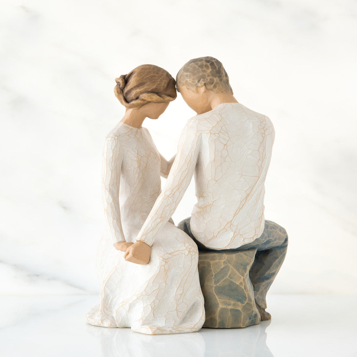 Man and woman figurine in white sitting on rock holding hands facing one another