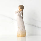 Left-faicng view, standing figure in cream dress, holding arms to face in wistful gesture. Hair and dress embellished with gold dots