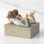 Back/left view of closed rectangular blue-gray resin box, sculpture of two girls affixed to lid