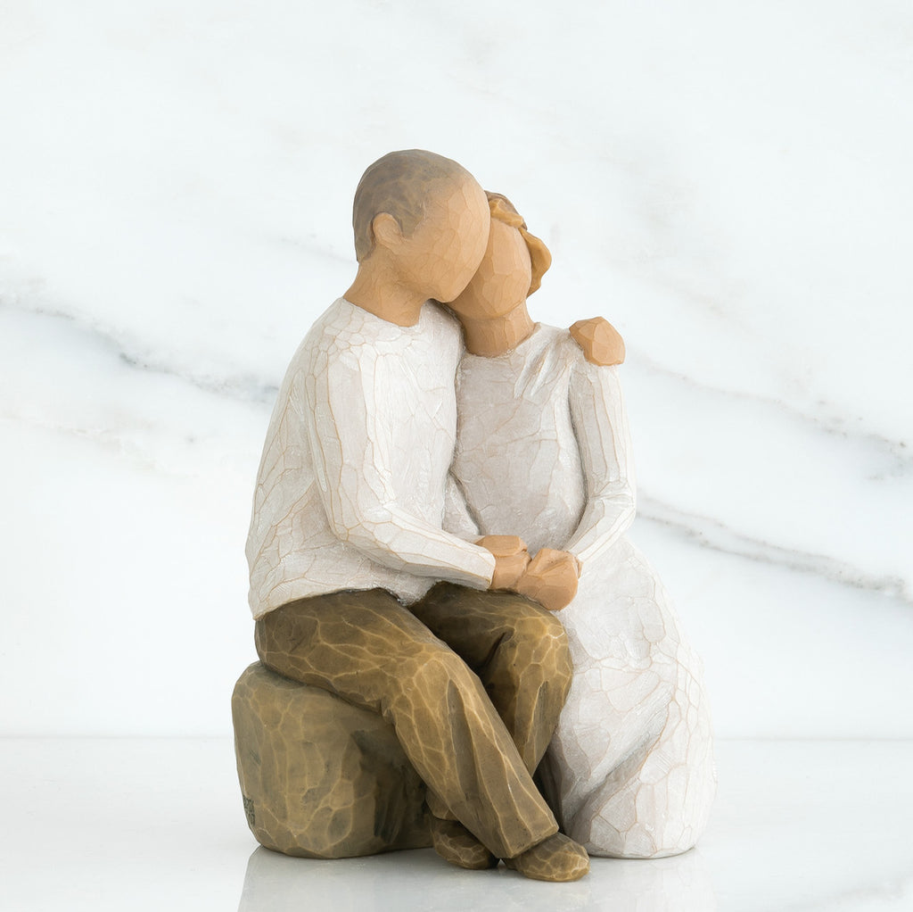 Man and woman figurines in white sitting on rock holding hands