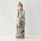 Brunette girl figurine in grey dress sitting on grey rock with her hands to her face