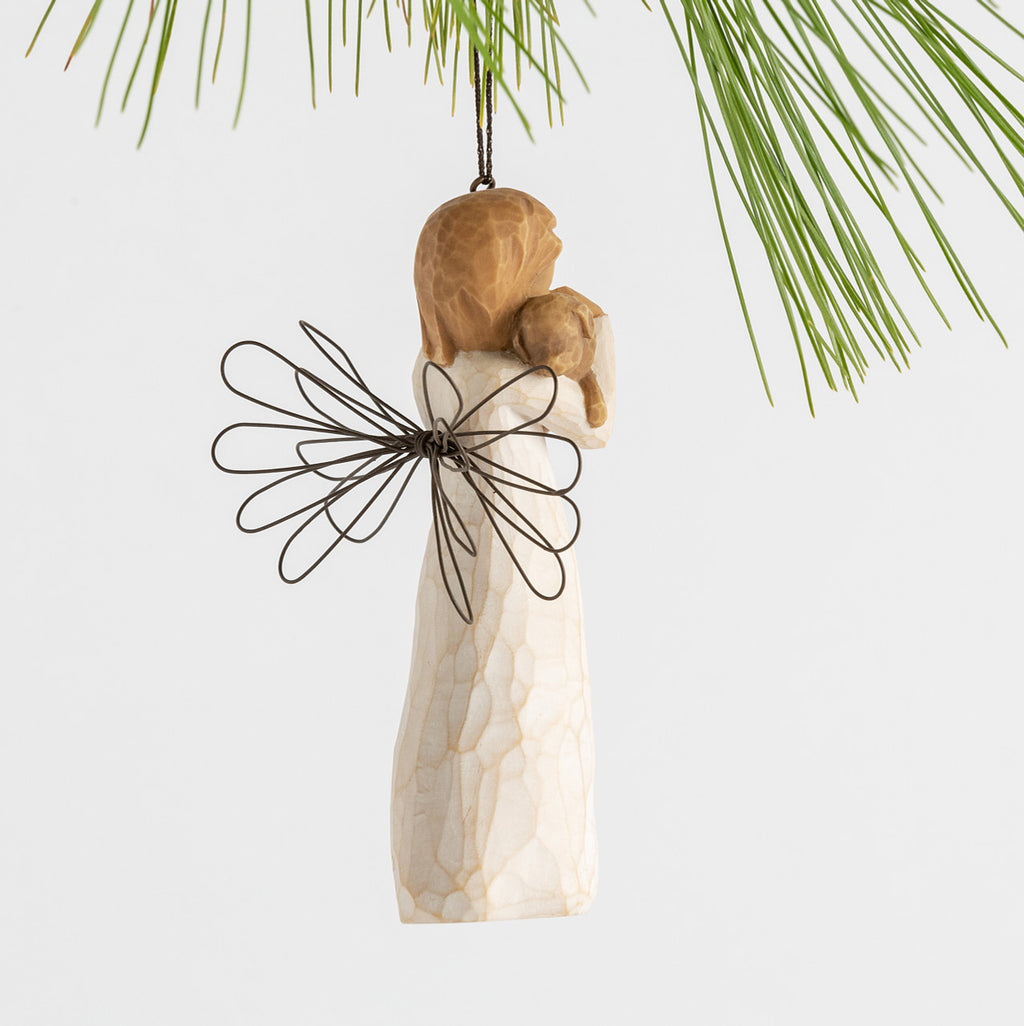 Side view female angel figure in cream dress with wire wings, holding brown dog in arms, ornament loop attached to head