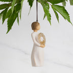 Facing right: Dated Ornament of figure holding pierced gold-leaf wreath of hearts. 2024 written on wreath; loop and hook in head