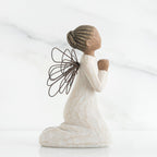 Side view of brunette angel figurine in white dress kneeling holding hands in prayer