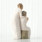 Back view, seated older female in cream dress, with younger female in cream dress, standing at her shoulder, hands embracing
