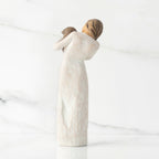Back view, standing female figure in cream dress, holding dark color puppy in her arms