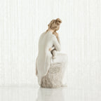 Woman figurine dressed in white sitting on rock holding baby - back view