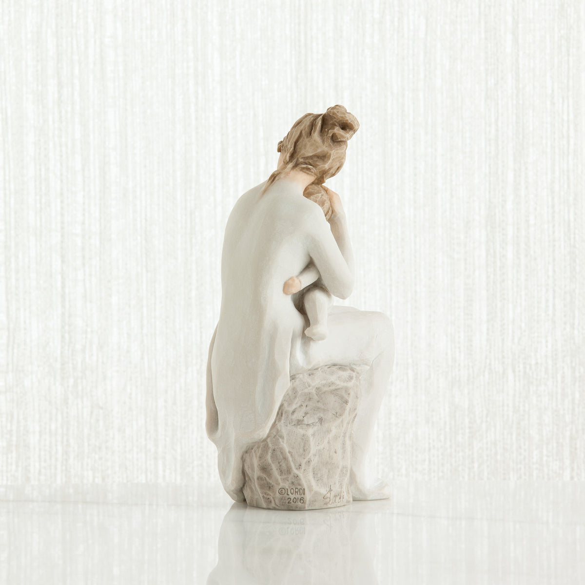 Woman figurine dressed in white sitting on rock holding baby - back view