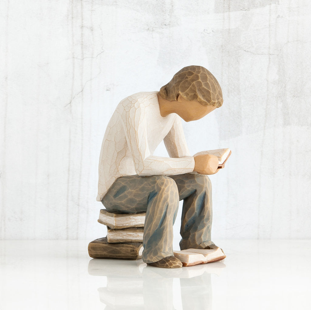 Side view of brunette boy in white shirt, blue jeans, sitting on book stack