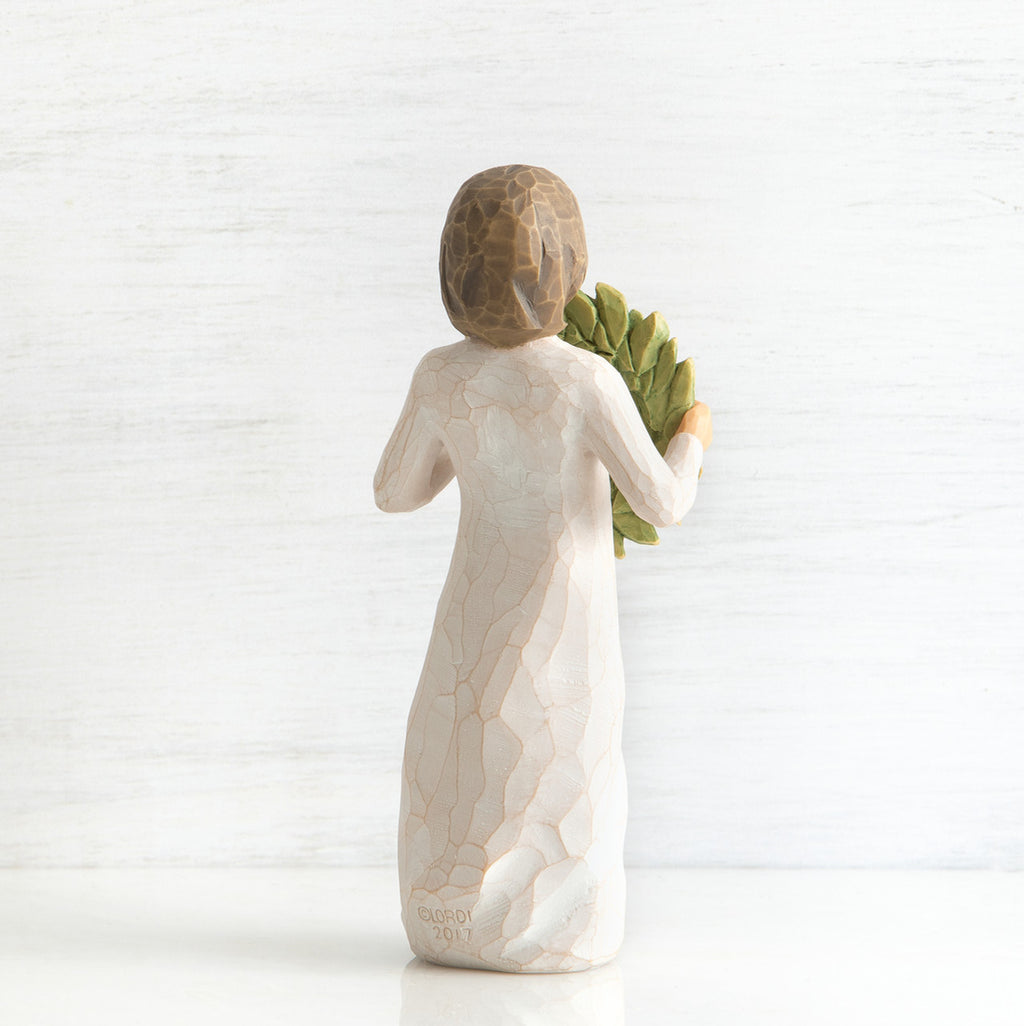 Back view of young girl with bangs and short brown hair holding up a green, leafy wreath