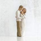 Man and woman figurines in white facing one another holding baby