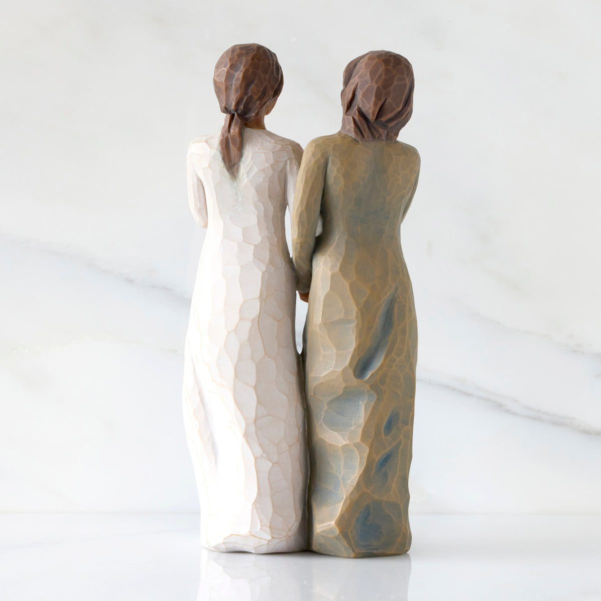 Back view: Figure of two women with darker skin tones in different colored dresses, standing arm in arm