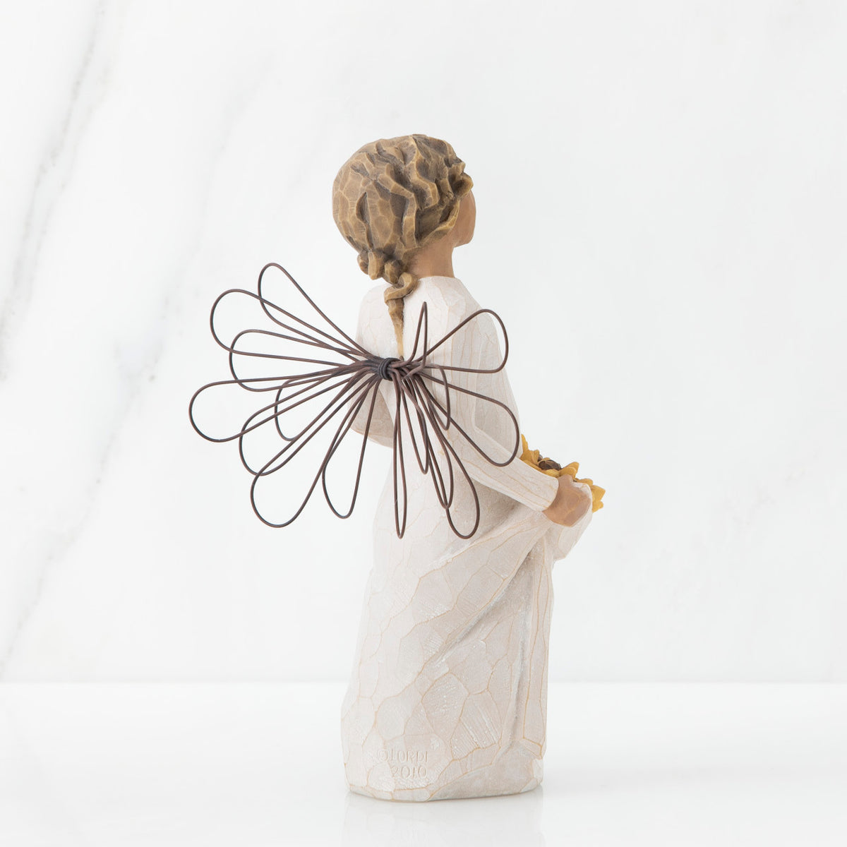 Back view of angel with tied back, curly, dark brown hair holding up a portion of her dress's skirt as it is full of sunflowers