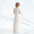 Back view of girl with brown hair in a bun holding three flowers with long stems up to her chest with both hands