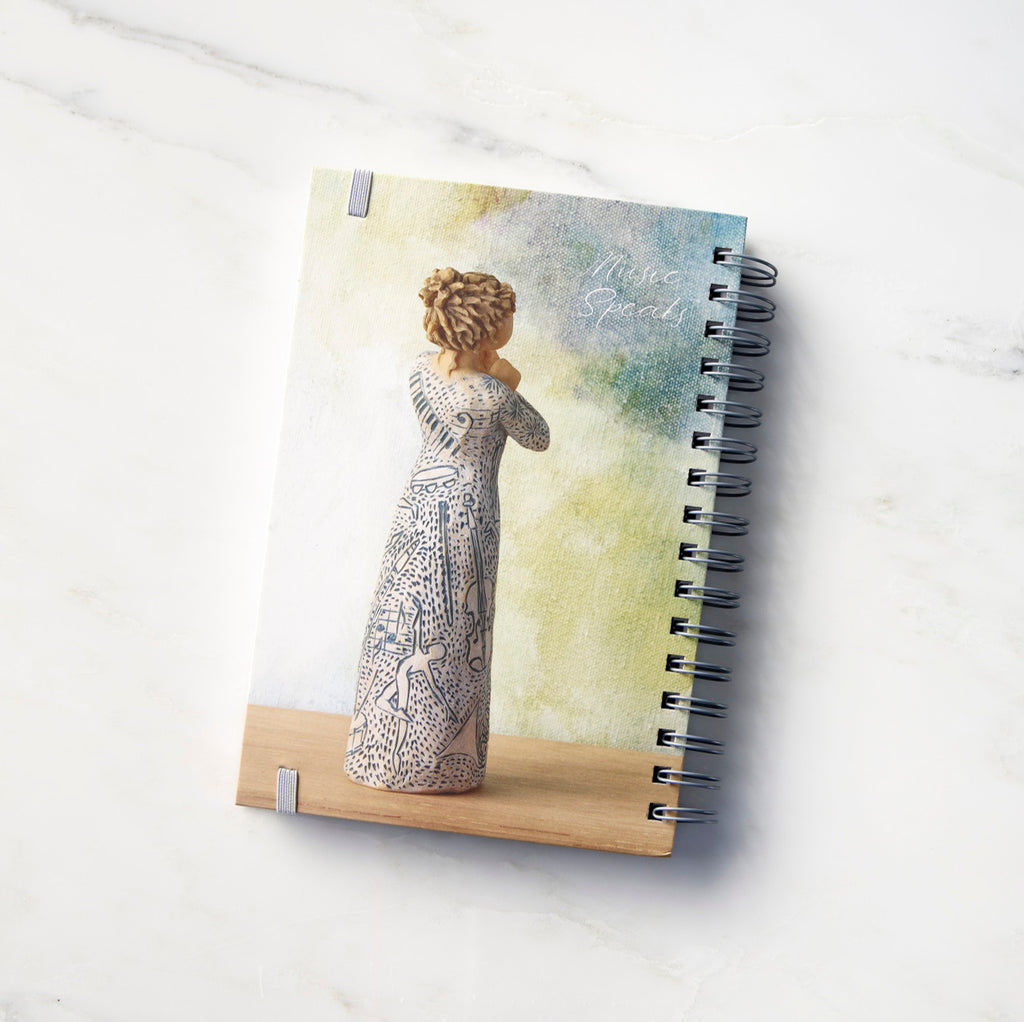 Back view: Spiral-bound notebook featuring back of female figure carved with contrasting pattern of dark blue musical symbols, instruments, dancing forms