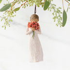 Figure in cream dress holding large bouquet of red-orange poppies up to face, ornament hook attached to head