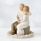 Man and woman figurine in white sitting on a rock on top of round white plaque hugging one another