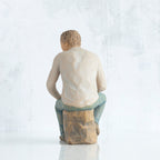 Back view, adult male figure in light gray shirt and blue jeans, seated on gray rock