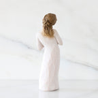 Back view: Standing figure in cream dress with hands to heart in empathetic gesture
