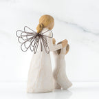 Blonde angel figurine in white dress, black wire wings, facing the back holding baby figurine's hands up