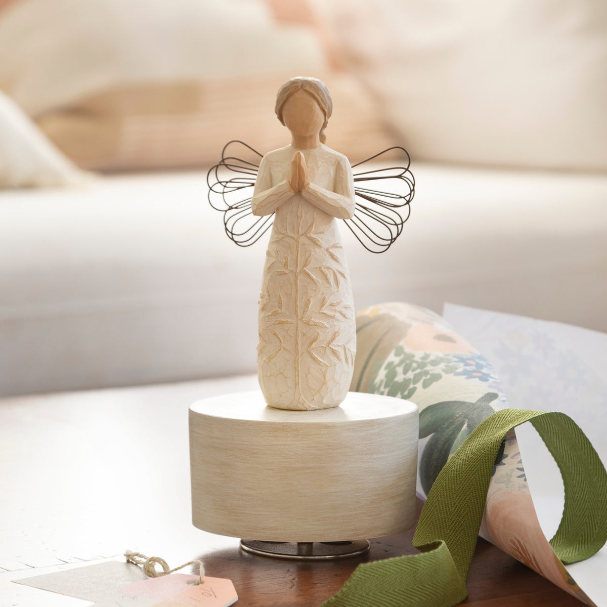 Willow Tree a tree, a prayer Musical, 7.5”h hand-painted resin angel figure in cream dress with wire wings, hands in prayer position, tree carving on dress, atop round, cream base containing musical element, on table with ribbon