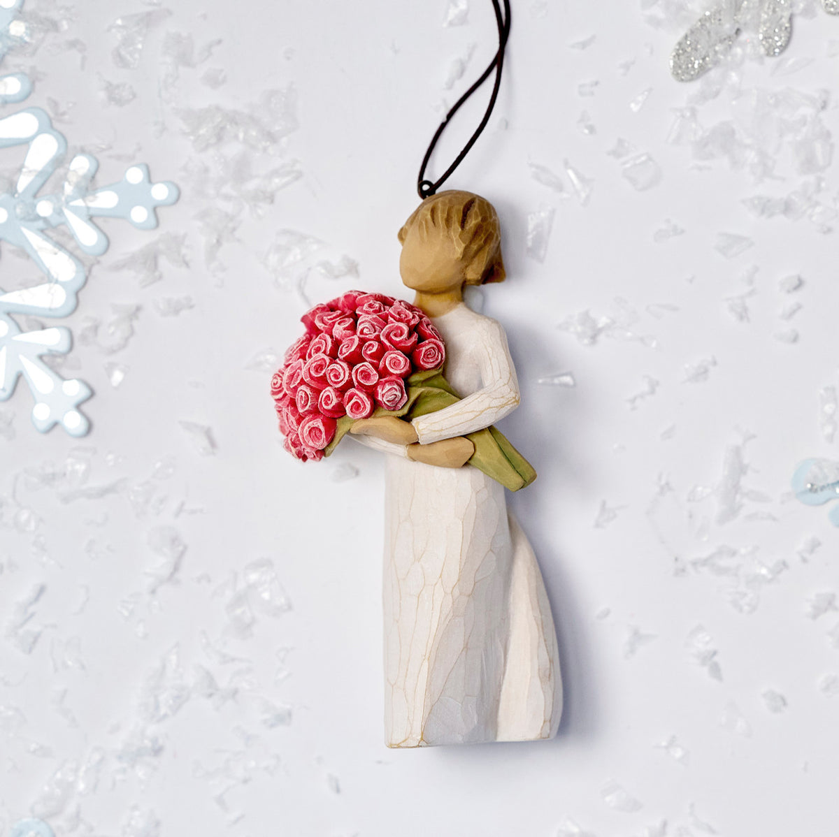 Willow Tree Abundance Ornament, 4”h hand-painted resin figure in cream dress, holding bouquet of pink roses, brown elastic cord, laying amongst snowflakes