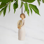 Facing left: Dated Ornament of figure holding pierced gold-leaf wreath of hearts. 2024 written on wreath; loop and hook in head