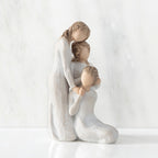 Right-facing view, figurine of three females in cream dresses: one standing with arm around kneeling female, and holding hand of seated female