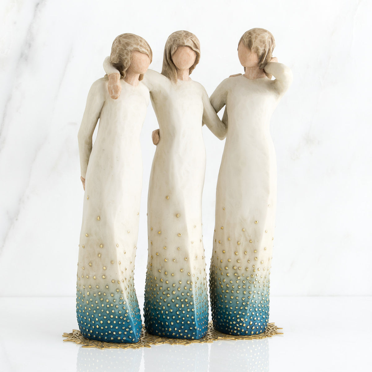 Three brunette woman figurines in white dresses blue bottoms facing forward with arms around each other
