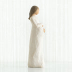 Side view of brunette girl figurine in white dress holding her stomach